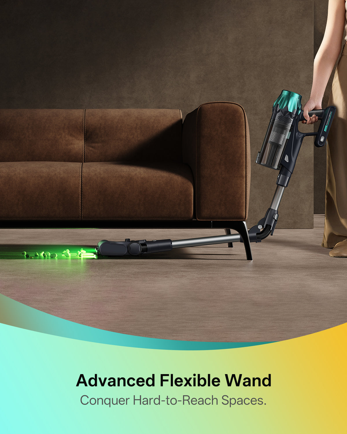 Person using a vacuum cleaner with an advanced flexible wand to clean under a brown sofa.